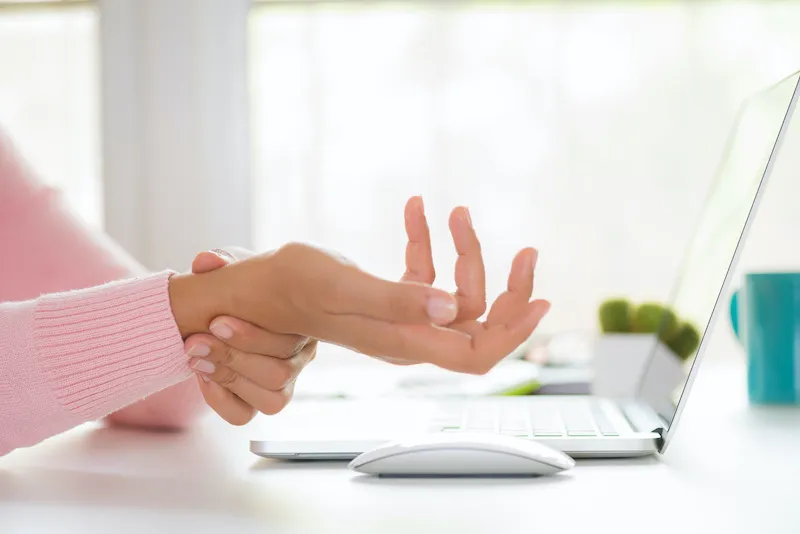 Person performing a gentle wrist stretch at their desk, hands extended with fingers pointing upward